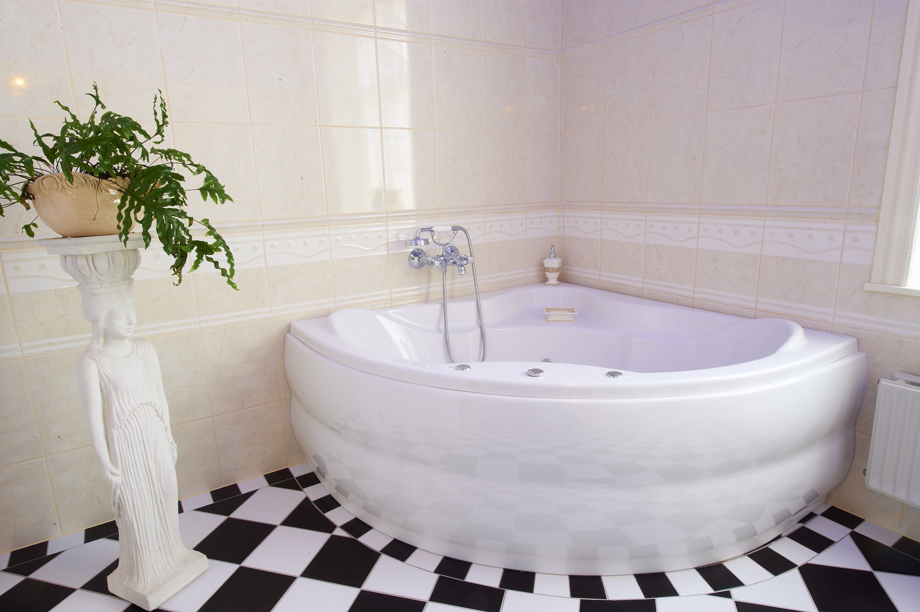 A bathroom with a freestanding bathtub, a pedestal with a plant, and a checkered floor.