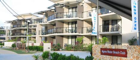 Un hotel de varios pisos con balcones, un cartel que indica 'NOW OPEN' y un letrero que dice 'Agnes Water Beach Club'.