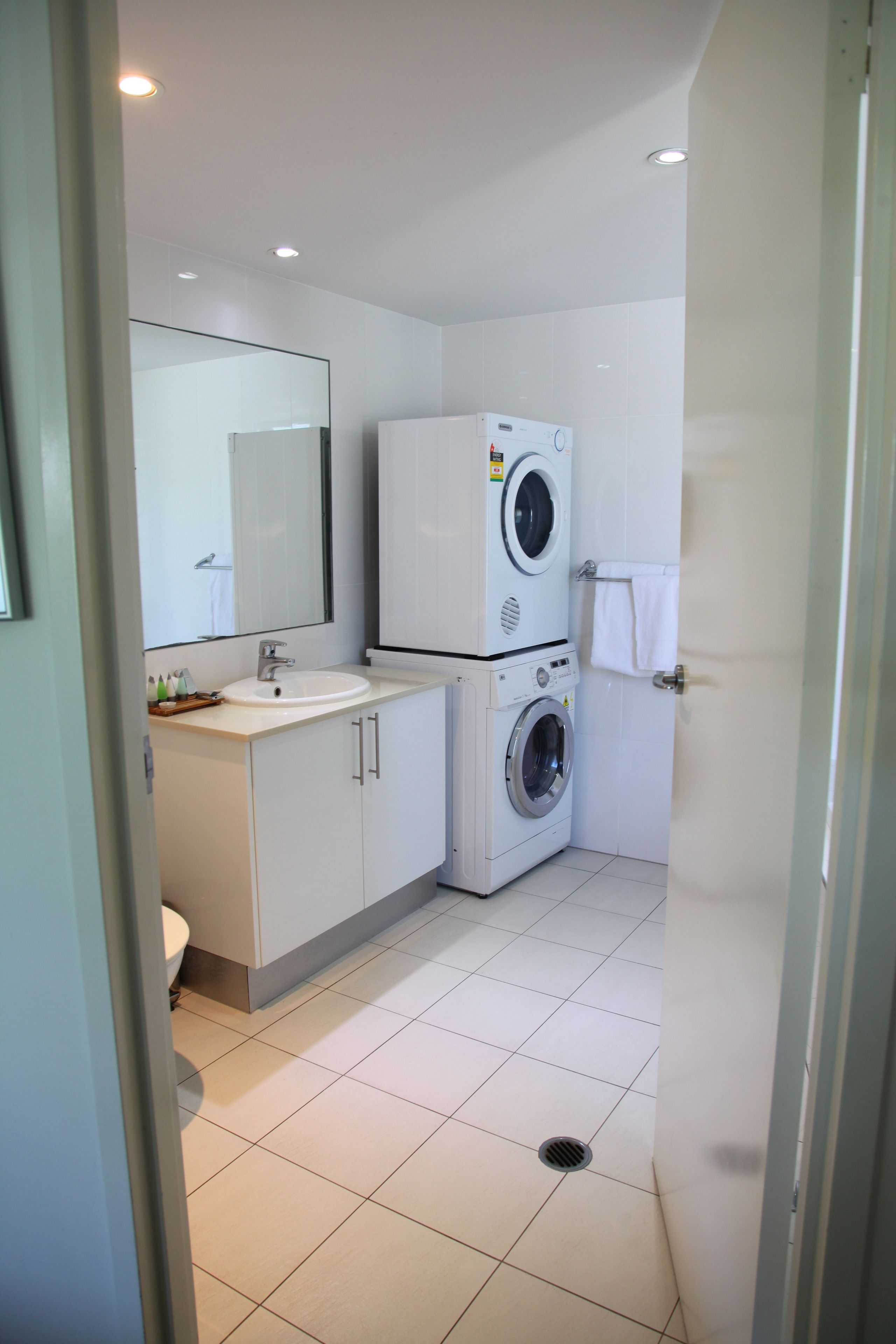 Une petite salle de bain comprenant un lavabo, un miroir et un lave-linge superposé.