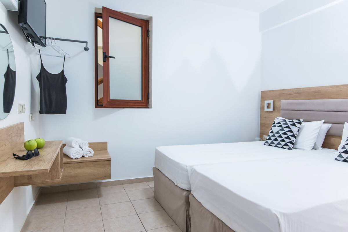 Ein Schlafzimmer mit einem Bett, einer hölzernen Bank mit Handtüchern und Äpfeln, einem Spiegel und einem Fenster.