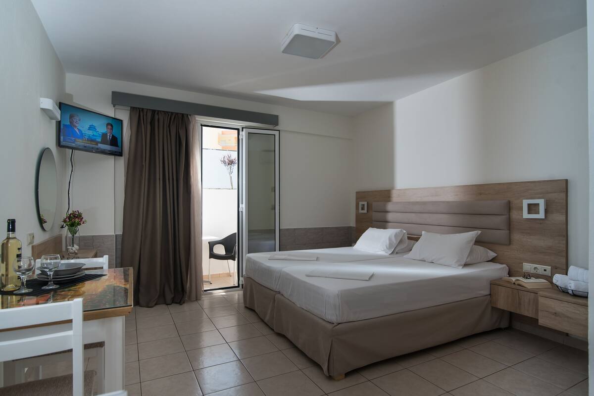 Ein Hotelzimmer mit einem Bett, einem Schreibtisch mit Stuhl, einem Fernseher und einer Glasschiebetür nach draußen.