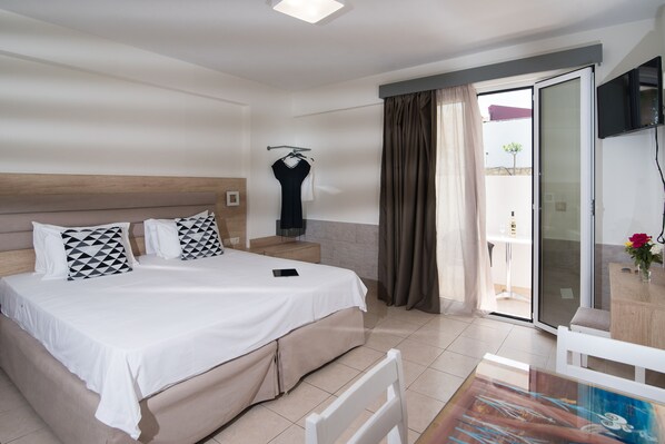 Habitación de hotel con cama, mesita de noche, televisor y vistas al balcón exterior.