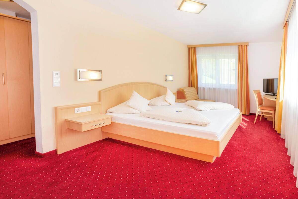 A hotel room with a large bed, a desk, a TV, and a wardrobe.