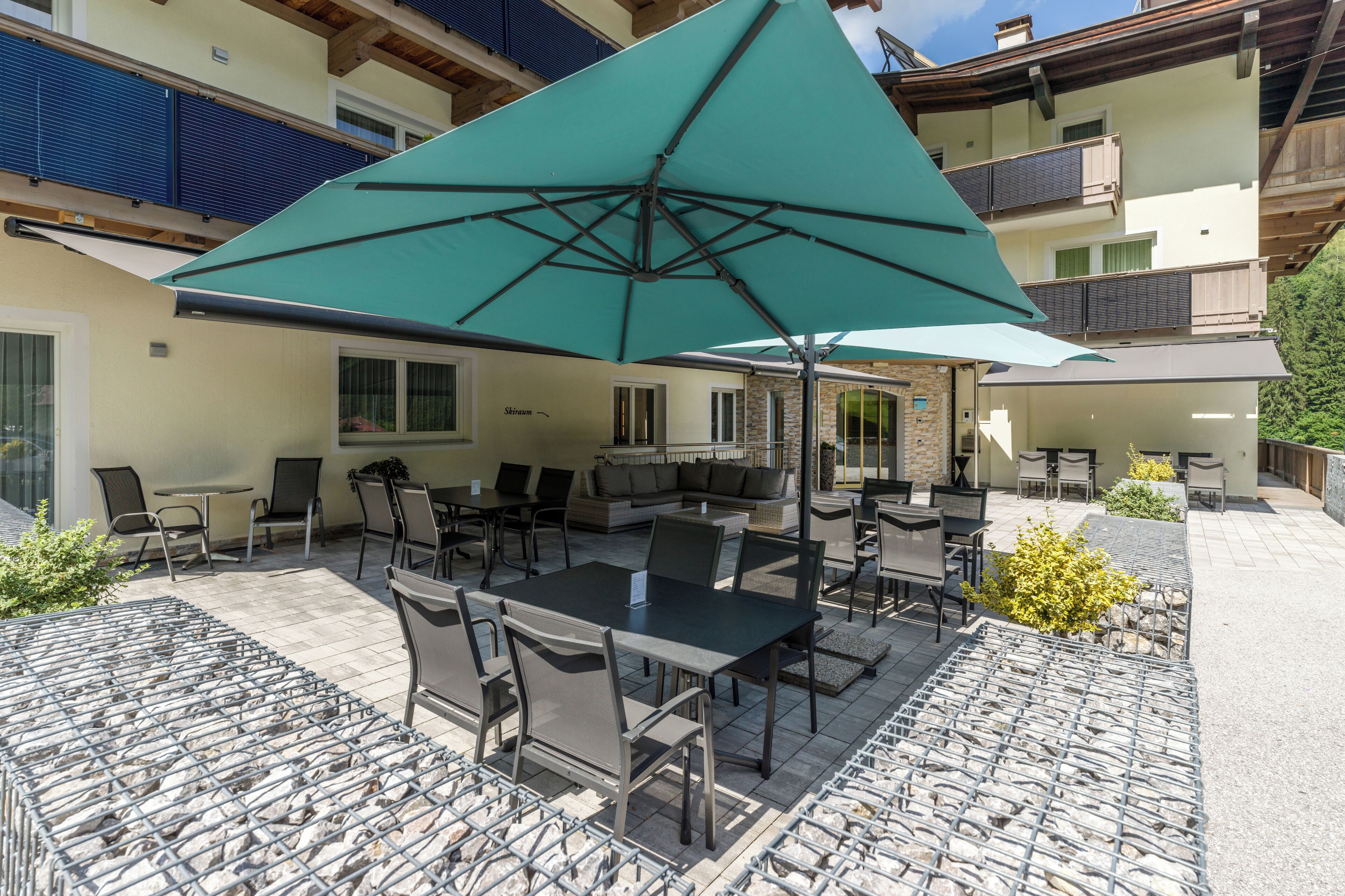 An outdoor patio area with tables and chairs, a large umbrella, and a stone-tiled floor.