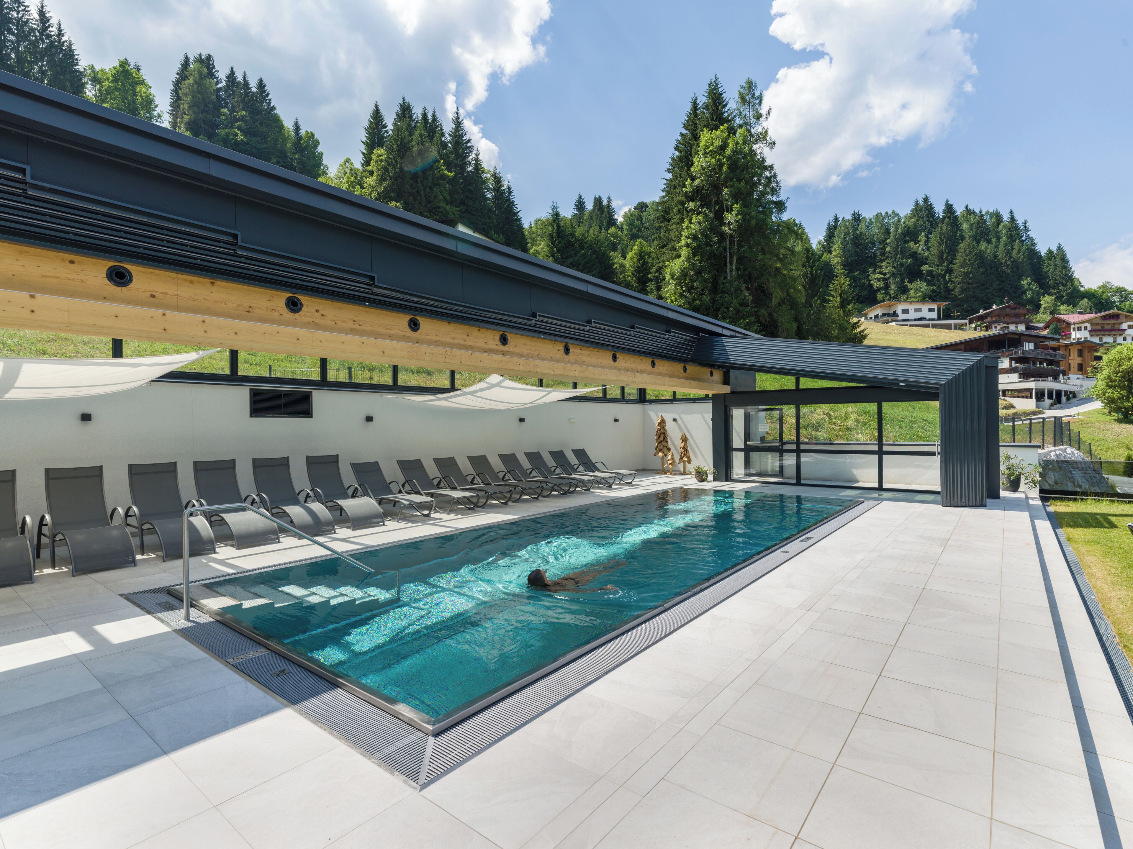 A swimming pool with a person swimming, surrounded by lounge chairs and a covered area.