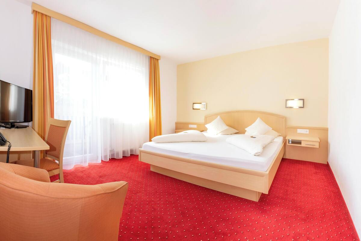 A hotel room with a bed, a desk, a chair, and a television.