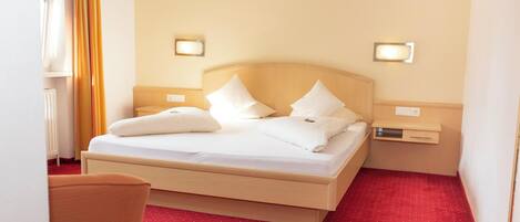 A hotel room with a bed, two bedside tables, a nightstand, and a red carpeted floor.