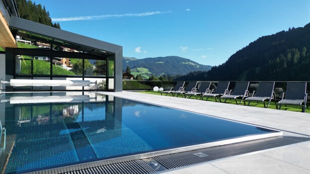 Ein moderner Poolbereich mit freiem Blick auf Berge und einem Haus im Hintergrund.