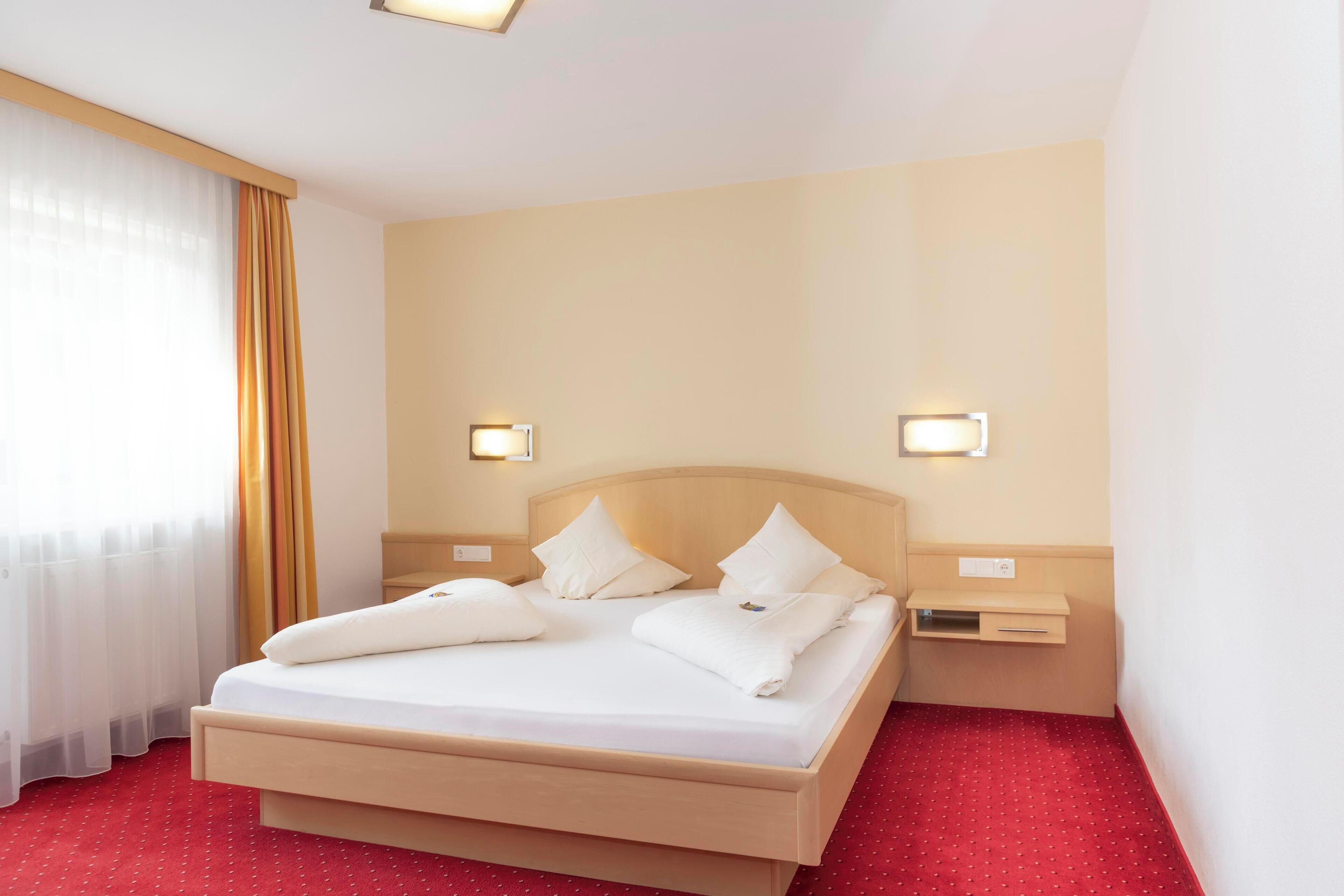 A hotel room with a bed, two bedside tables, and a window with curtains.