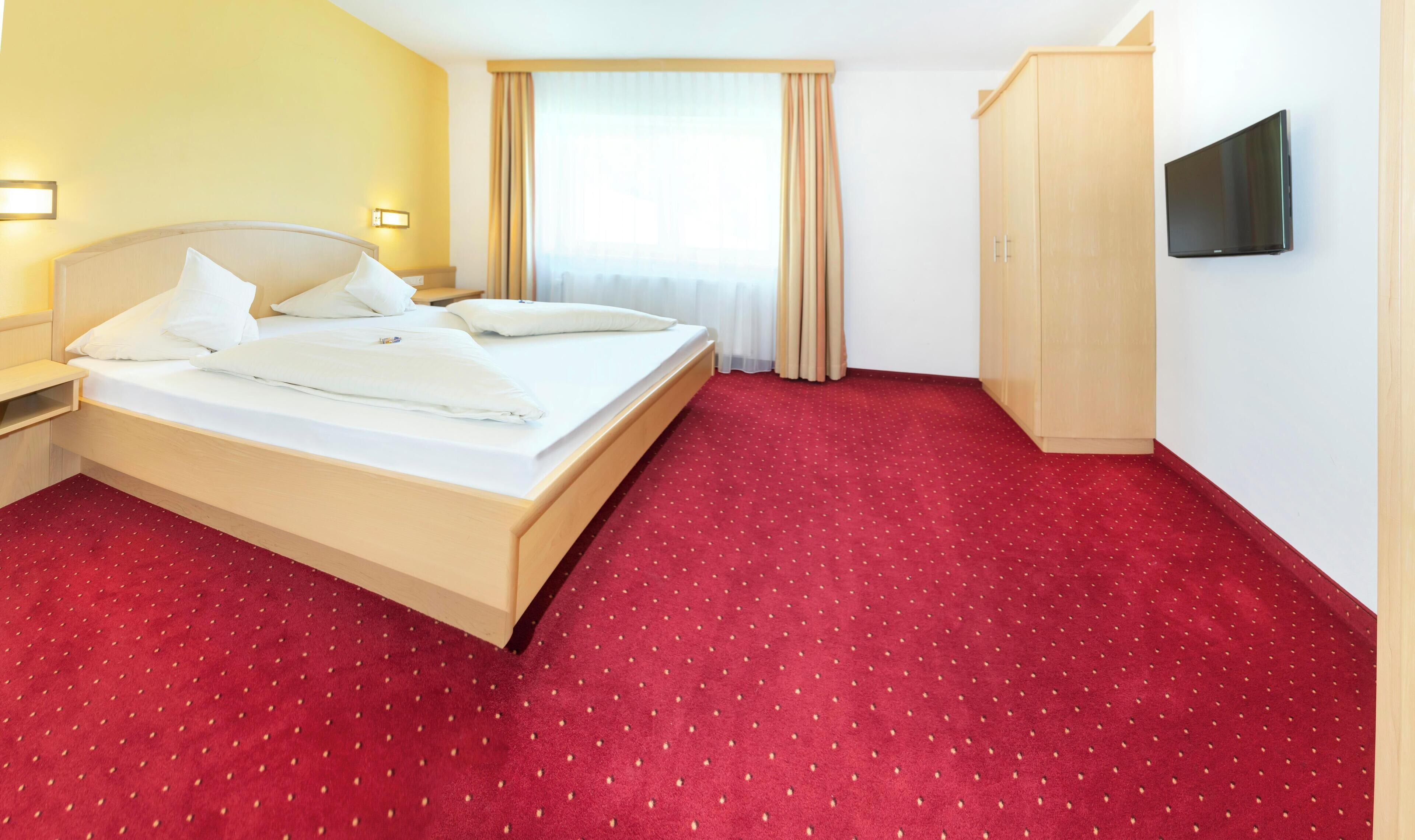 Una camera d'albergo con un letto grande, un armadio, una televisione e una finestra con tende.