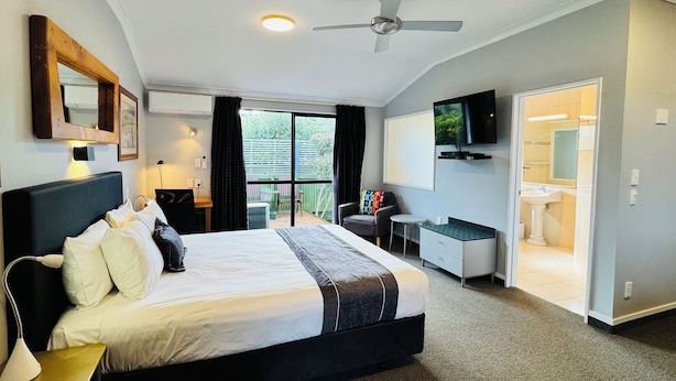 Ett modernt hotellrum med en stor säng, ett skrivbord, en TV och en balkong med utsikt över grönområden.