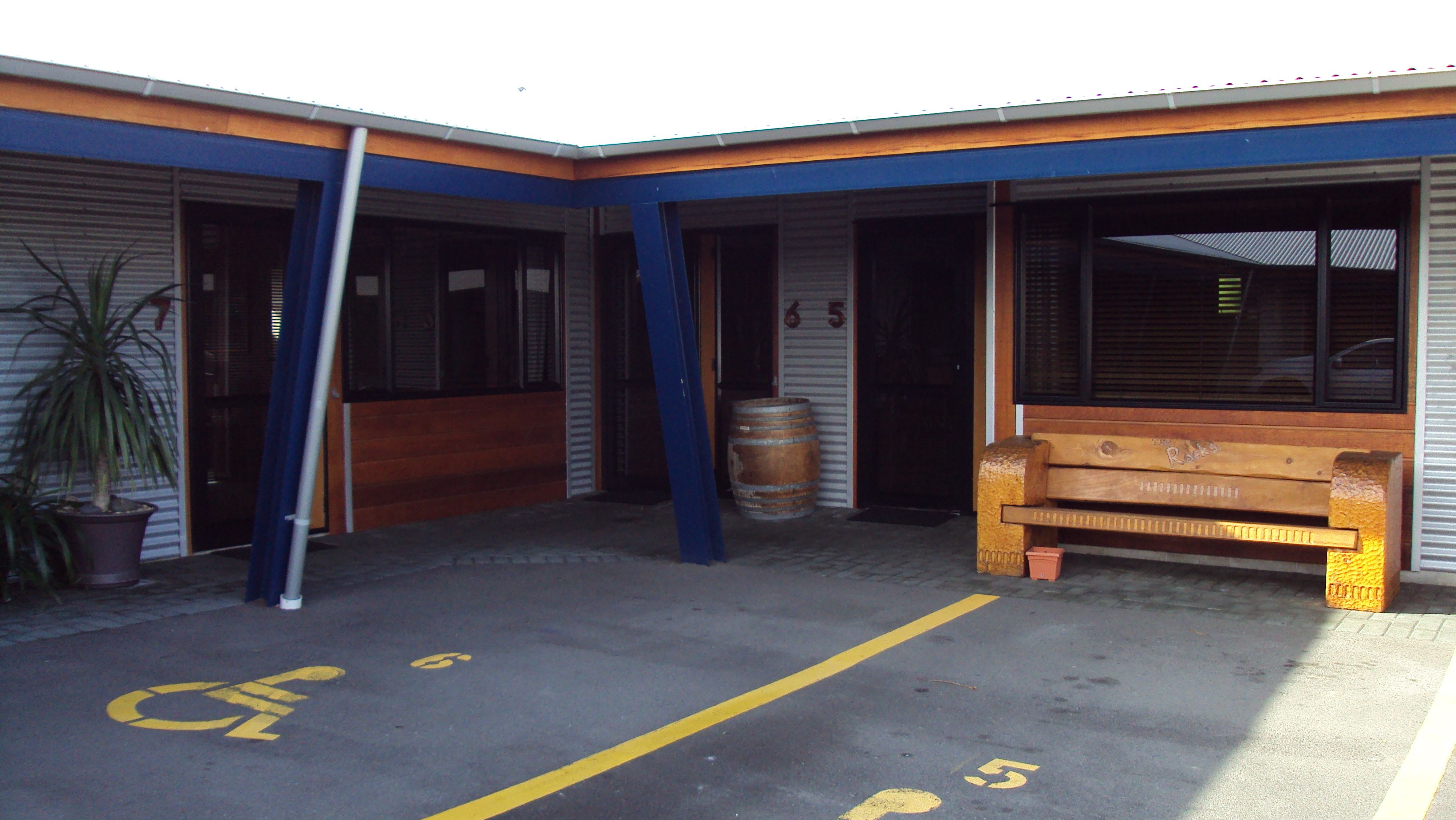 A building with a blue and orange facade, a wooden bench, a potted plant, and a wheelchair-accessible parking space.