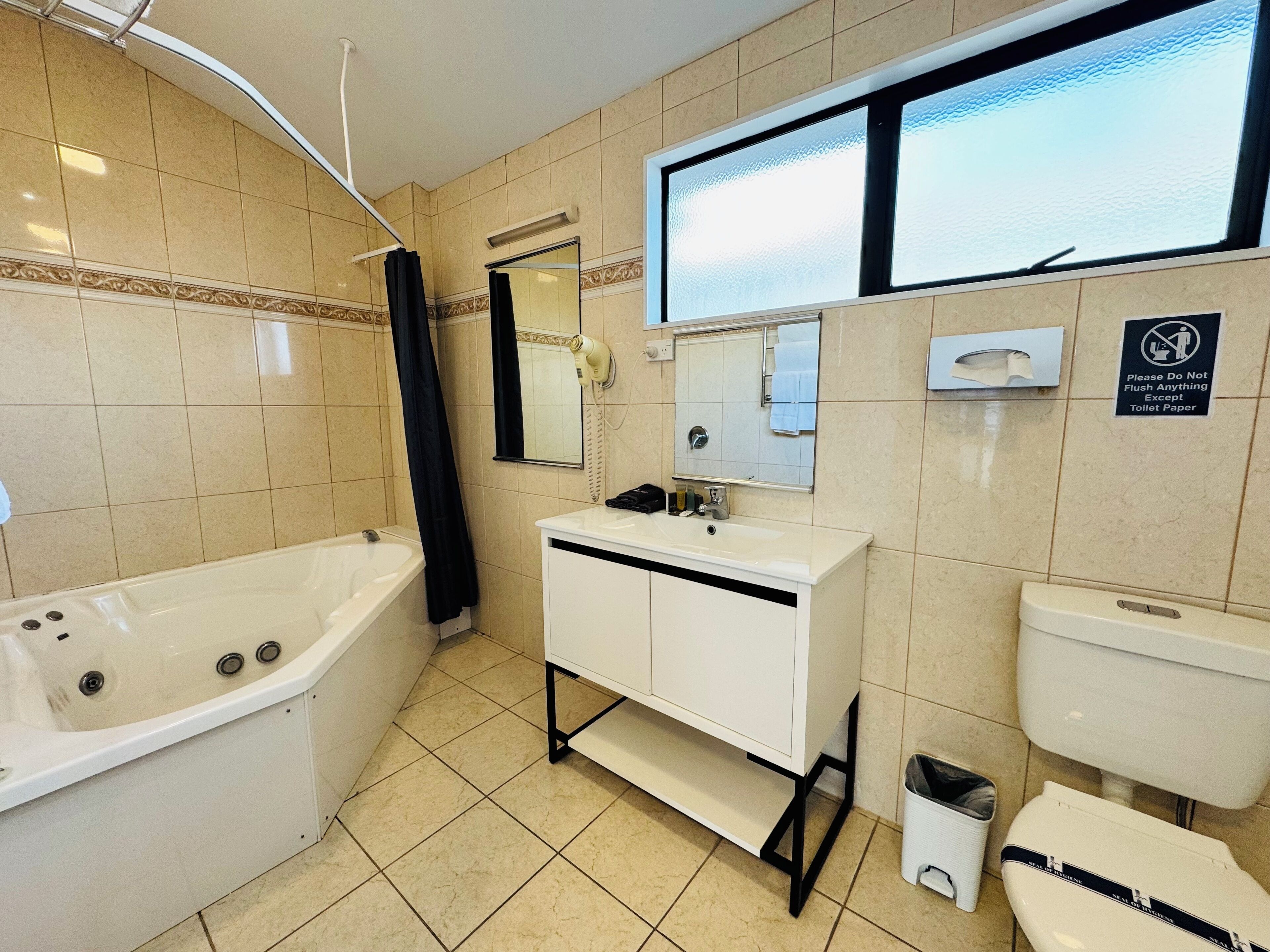 Un baño con bañera, lavamanos, inodoro, espejo y ventana.