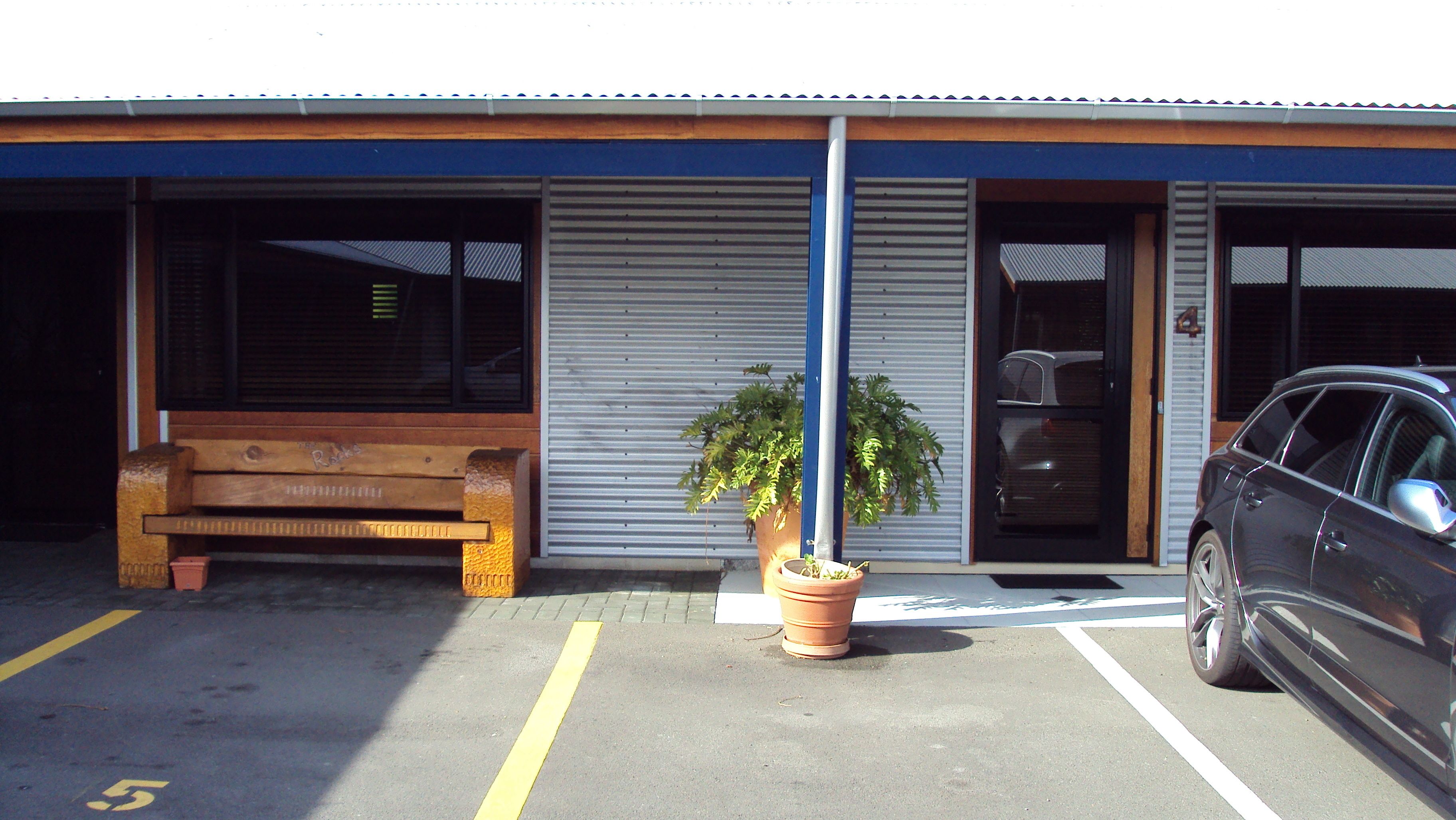 A parking area with a bench, a potted plant, and a car parked in front of a building with a blue awning and a number '4' sign.