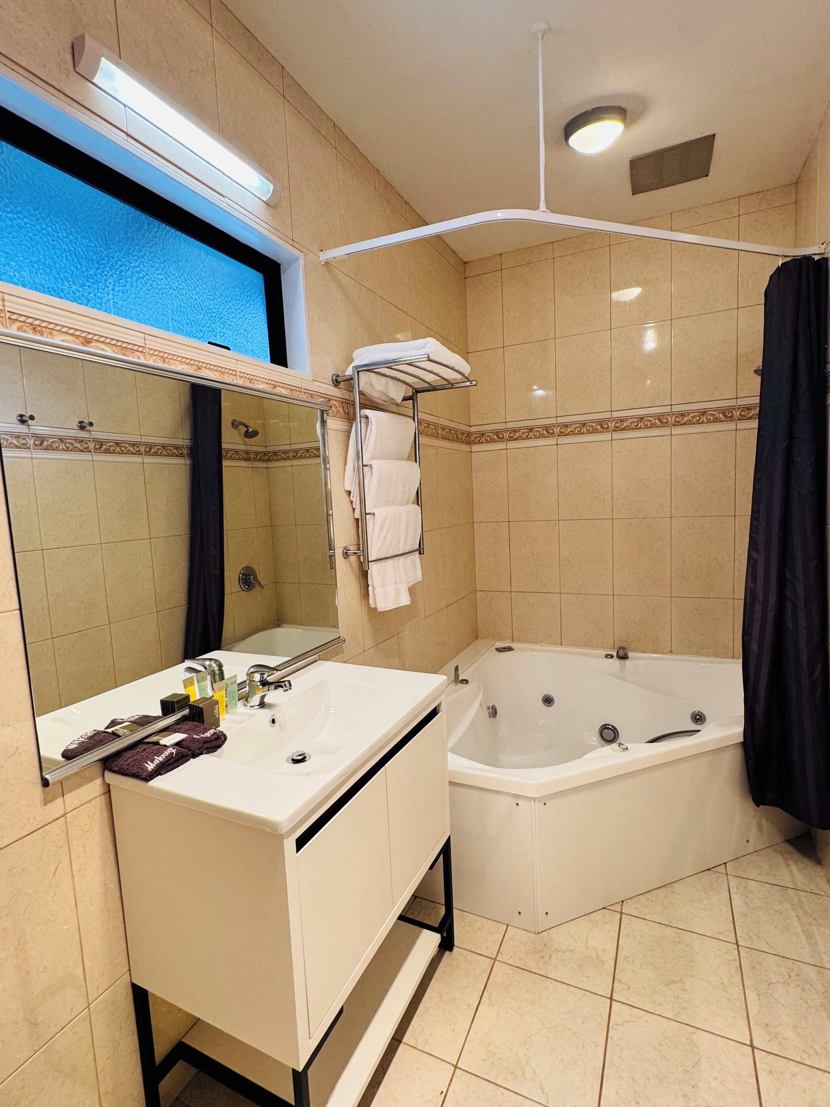 Un baño con bañera, lavamanos, espejo y perchero para toallas.