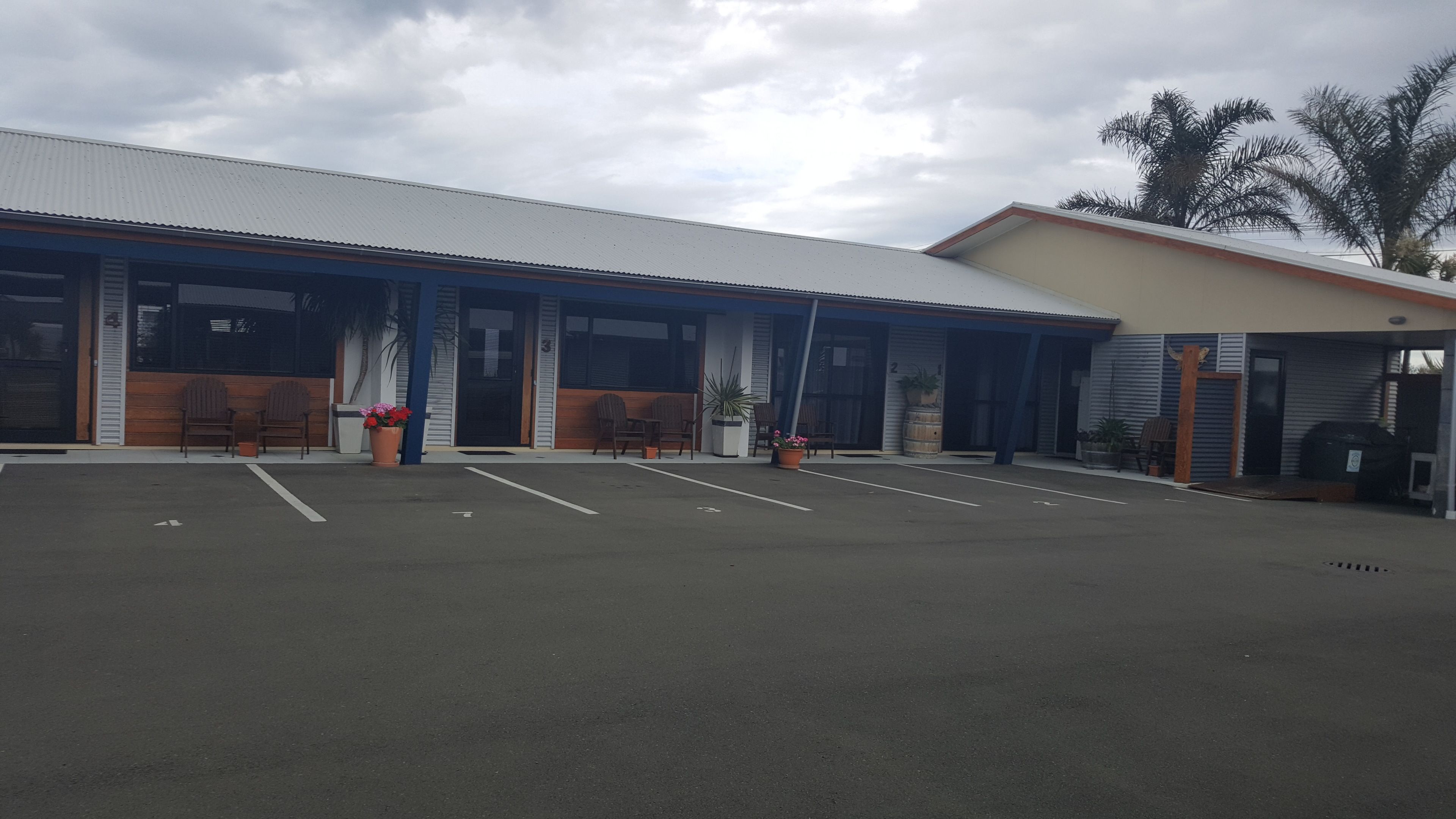 Un edificio con zona de estacionamiento techada, varias entradas y mesas al aire libre.
