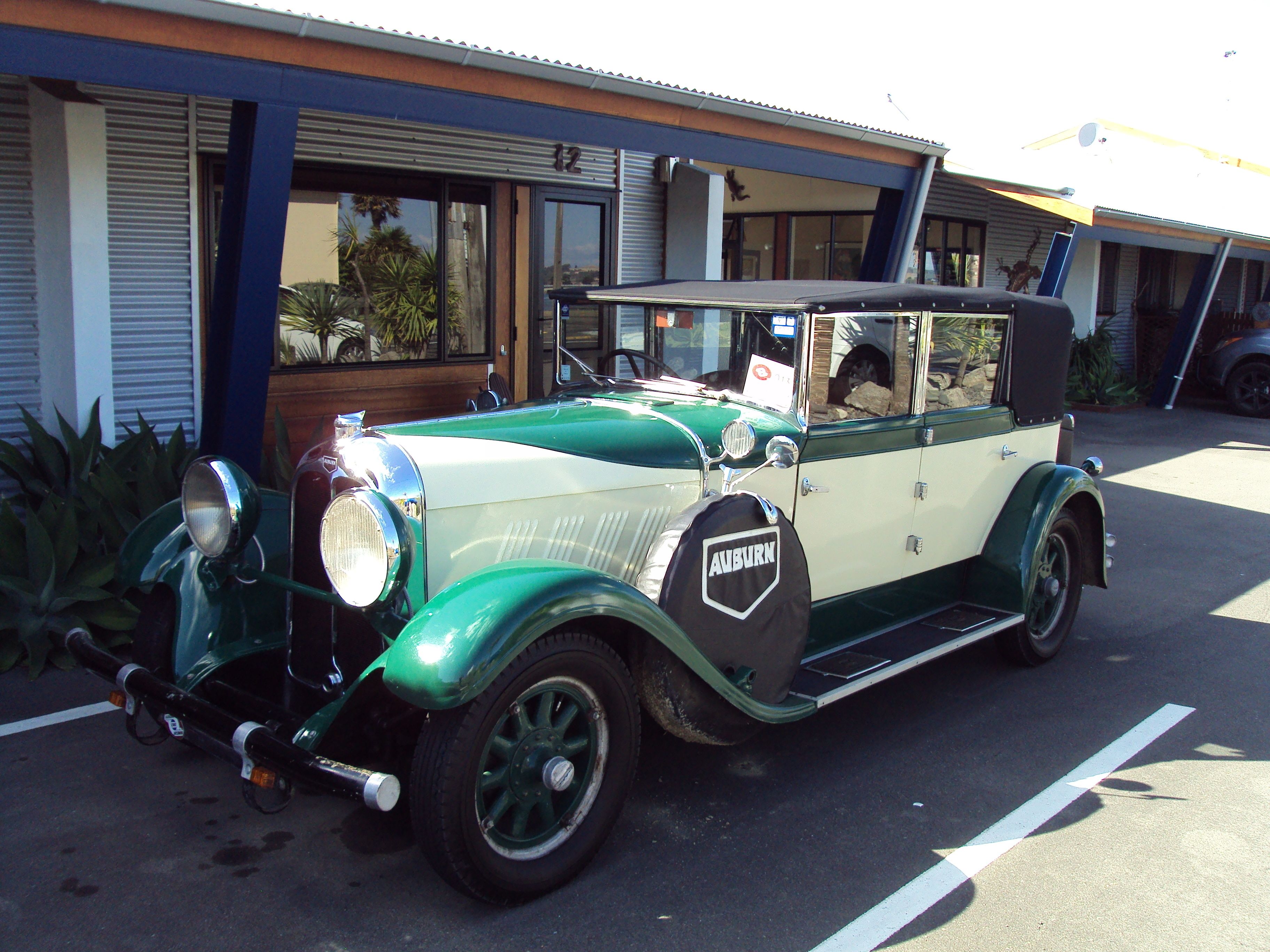 A vintage green and white car parked in front of a building with a blue and white facade.