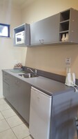 Una cocina compacta con microondas integrado, un lavamanos de acero inoxidable y un refrigerador Samsung.