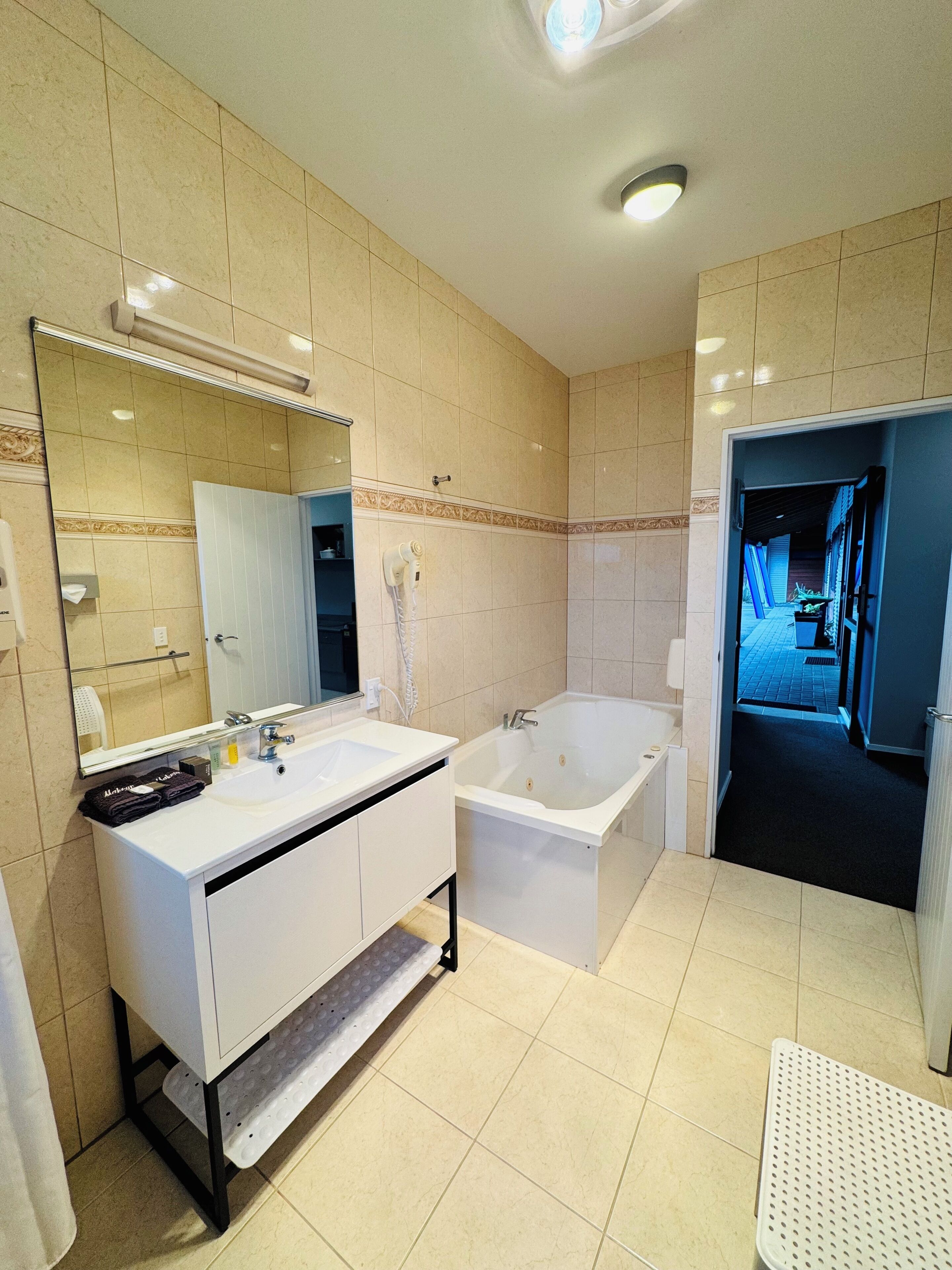 Un baño moderno con tocador blanco, un espejo grande, una bañera y una zona de ducha.