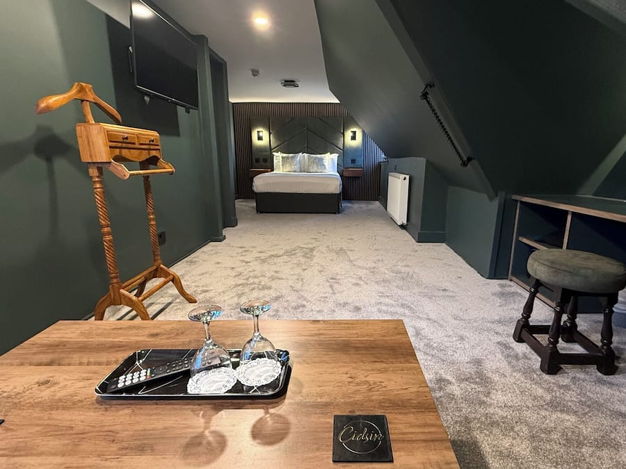 Un dormitorio moderno con techo inclinado, una mesa de madera con bandeja, una silla colgante, una mesita de noche y una cama con cabecera.