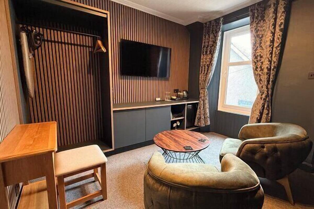 Uma sala de estar moderna com uma mesa de madeira, um sofá, uma TV fixada na parede e uma janela com cortinas.