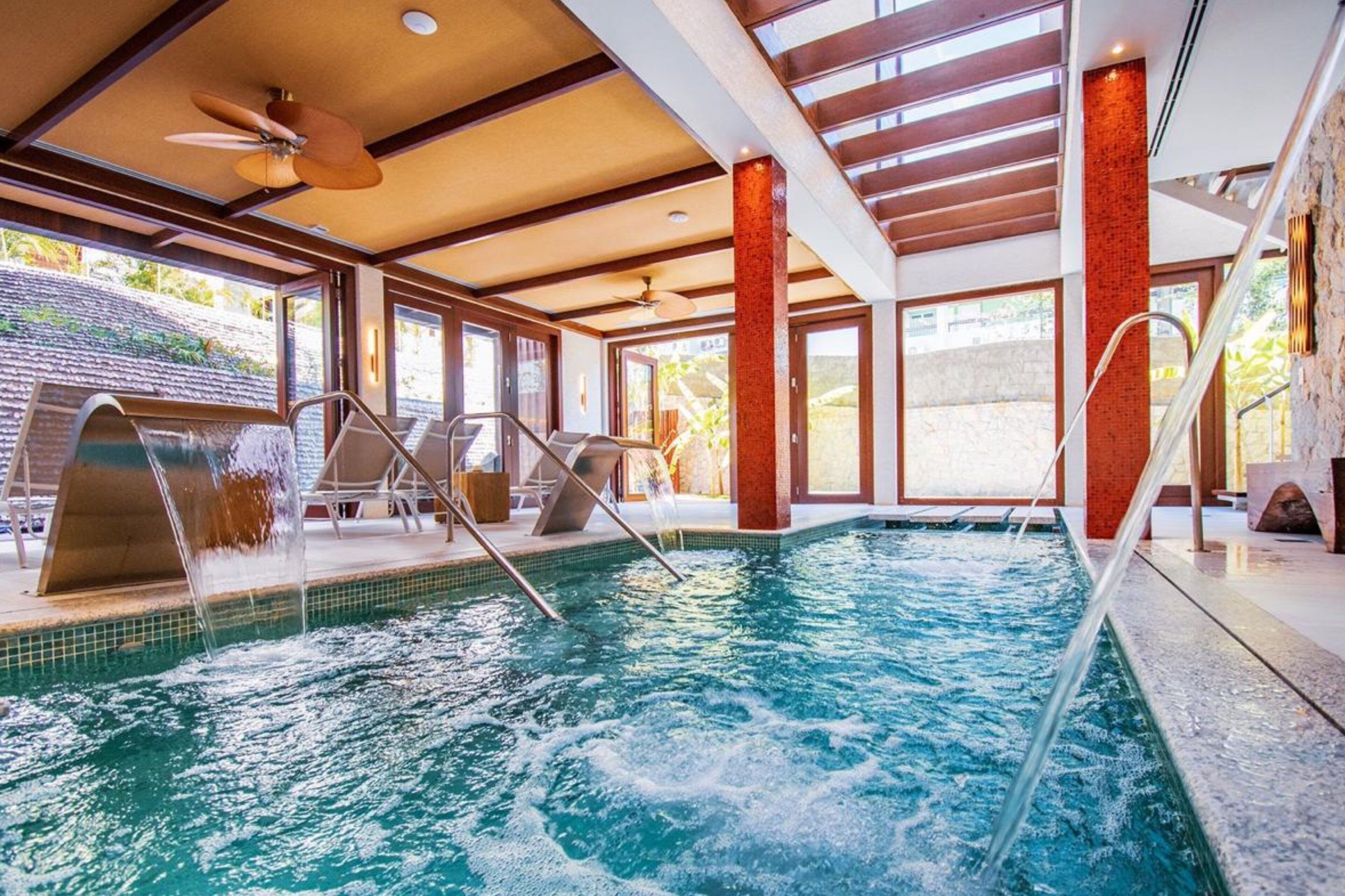 A swimming pool with a waterfall feature, surrounded by lounge chairs and a staircase.