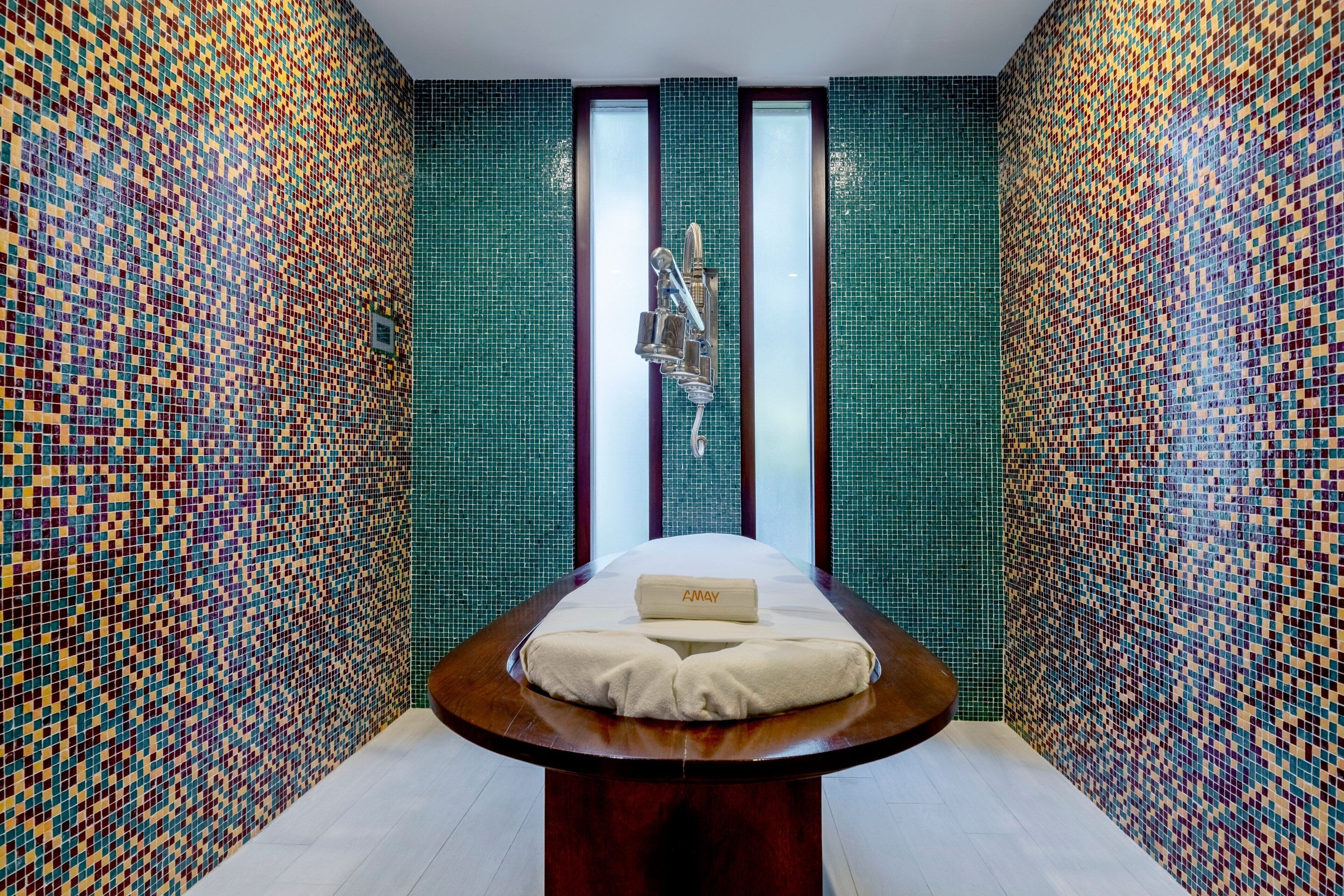 Une salle de spa avec un mur recouvert de mosaïques, une table de massage et une grande fenêtre.