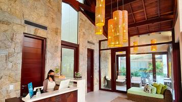 Un área de recepción con pared de piedra, mostrador de madera y zona de estar con sofá de fibras naturales.