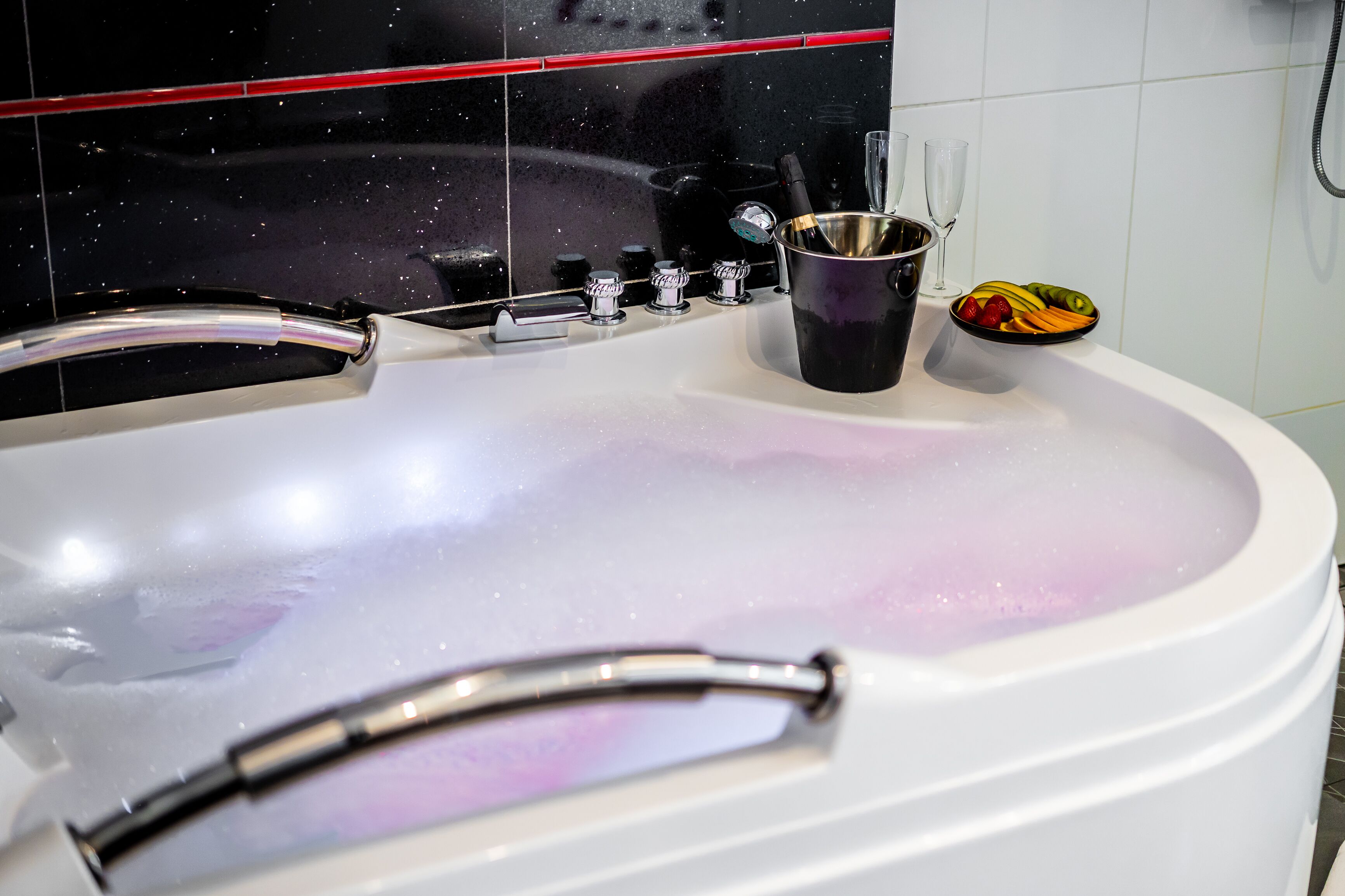 A bathroom with a white bathtub, a black container with a bottle, and a fruit bowl on the edge.