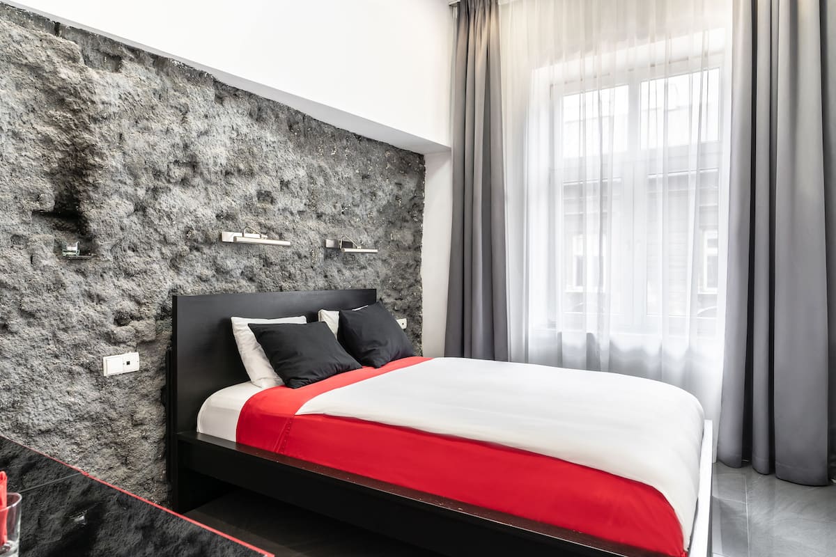 A modern bedroom with a textured wall, a bed with a red and white bedspread, and a window with sheer curtains.