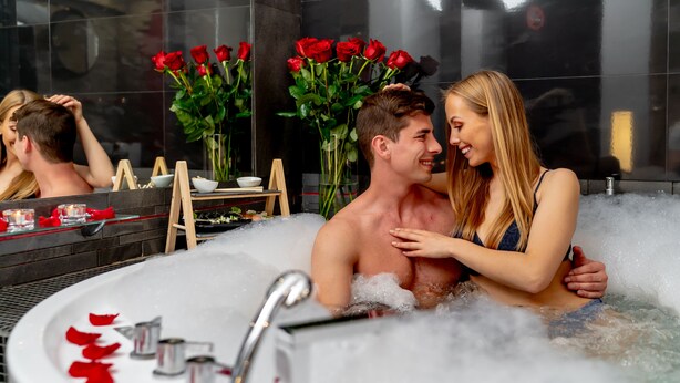 A couple in a bathtub with rose petals and a bouquet of roses.