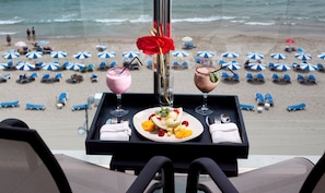 A table with a dessert and two drinks, overlooking a beach with umbrellas and lounge chairs. - Hotel Allon Mediterrània (Villajoyosa)