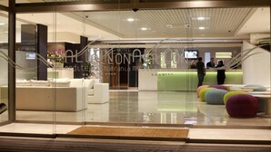 Een hotellobby met een receptiebalie, een zithoek en een glazen ingang.