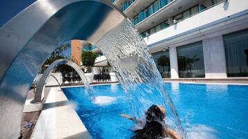 A swimming pool with a water feature, surrounded by a modern building with large windows.