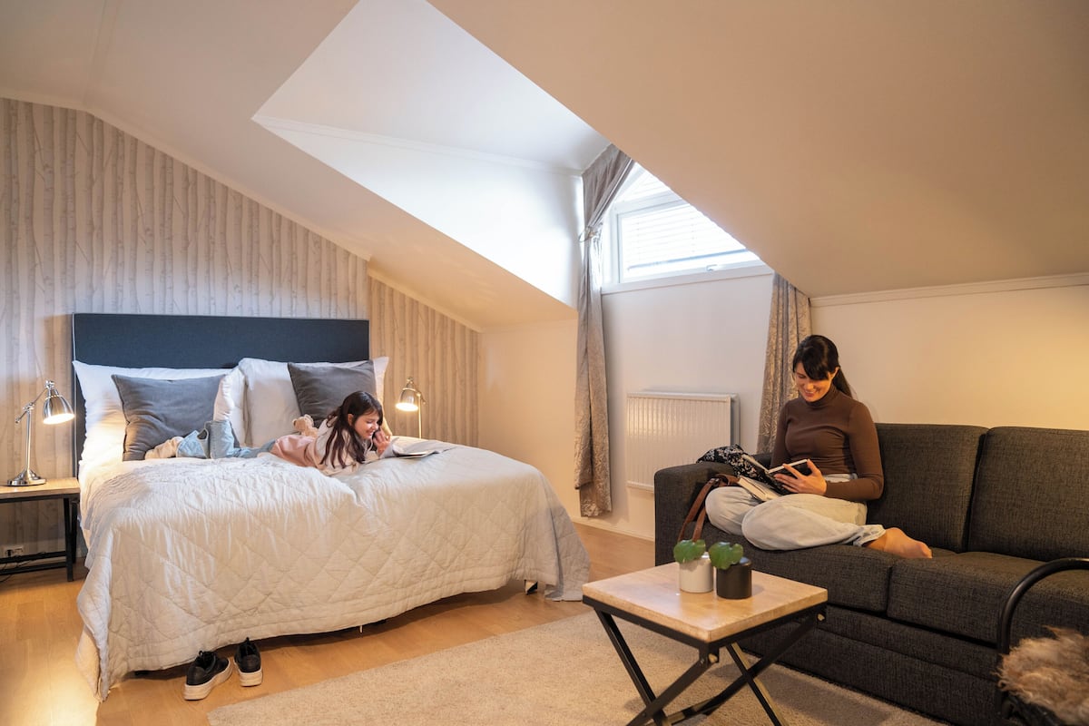 A bedroom with a bed, a sofa, a small table, and a window.
