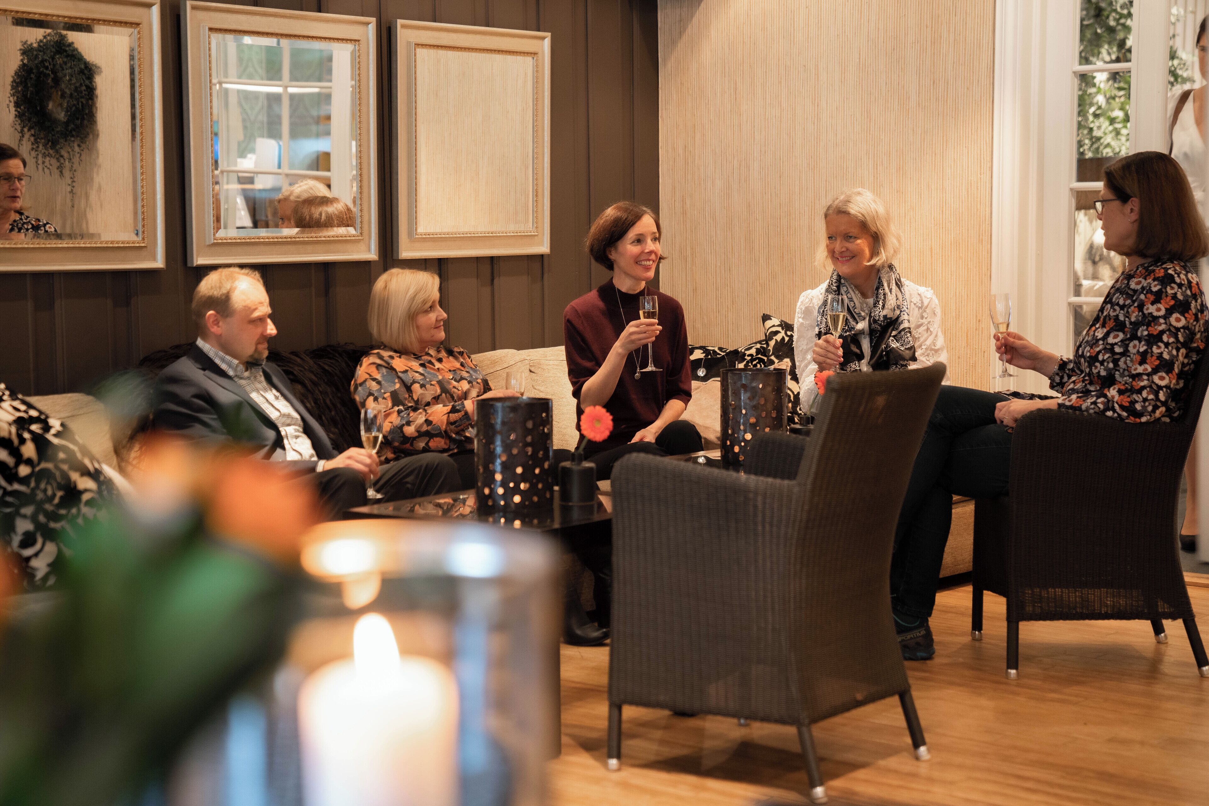 A group of people seated in a room with wooden floors and walls, engaged in conversation.