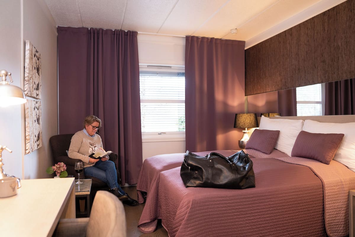 A hotel room with a bed, a chair, a desk, and a window with curtains.
