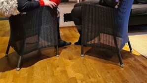 To personer sidder i fletstole og ser på en pejs med en dekorativ krans over.