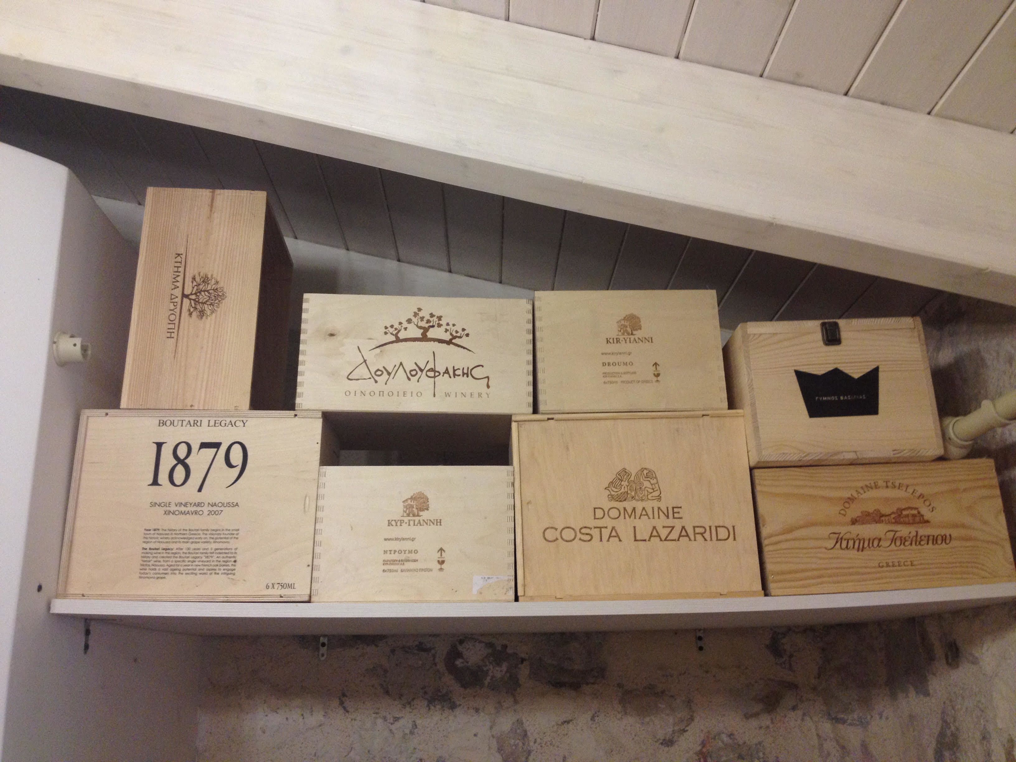 Une étagère en bois sur laquelle sont disposées différentes caisses de vin, chacune portant une étiquette indiquant le nom et l’année.