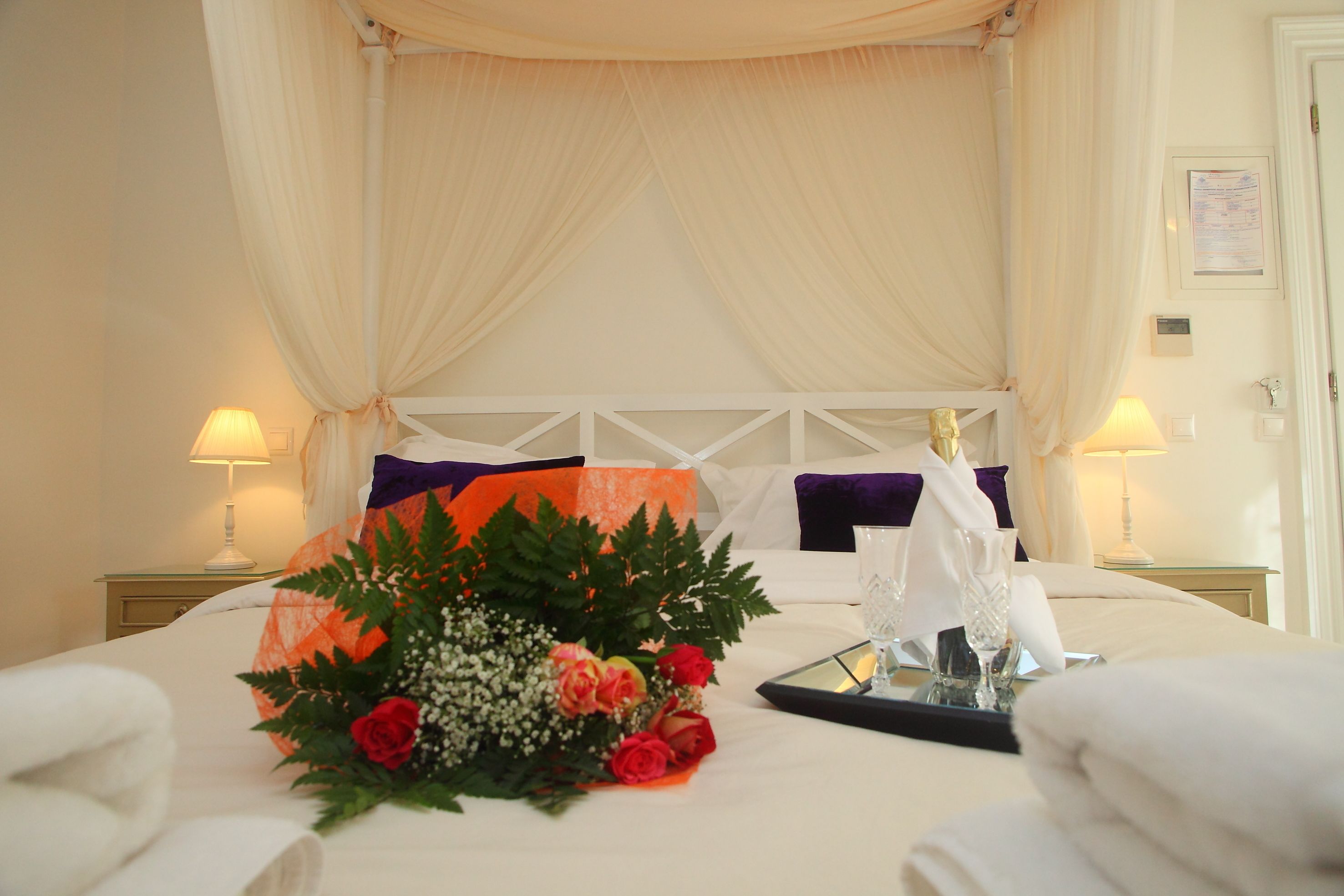 Quarto de hotel com cama grande, estrutura de dossel e mesa de cabeceira com abajur.
