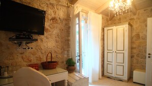 Une pièce avec un mur en pierre, un téléviseur à écran plat fixé au-dessus d’un bureau, une chaise blanche, un meuble blanc, une plante en pot et une grande armoire blanche.