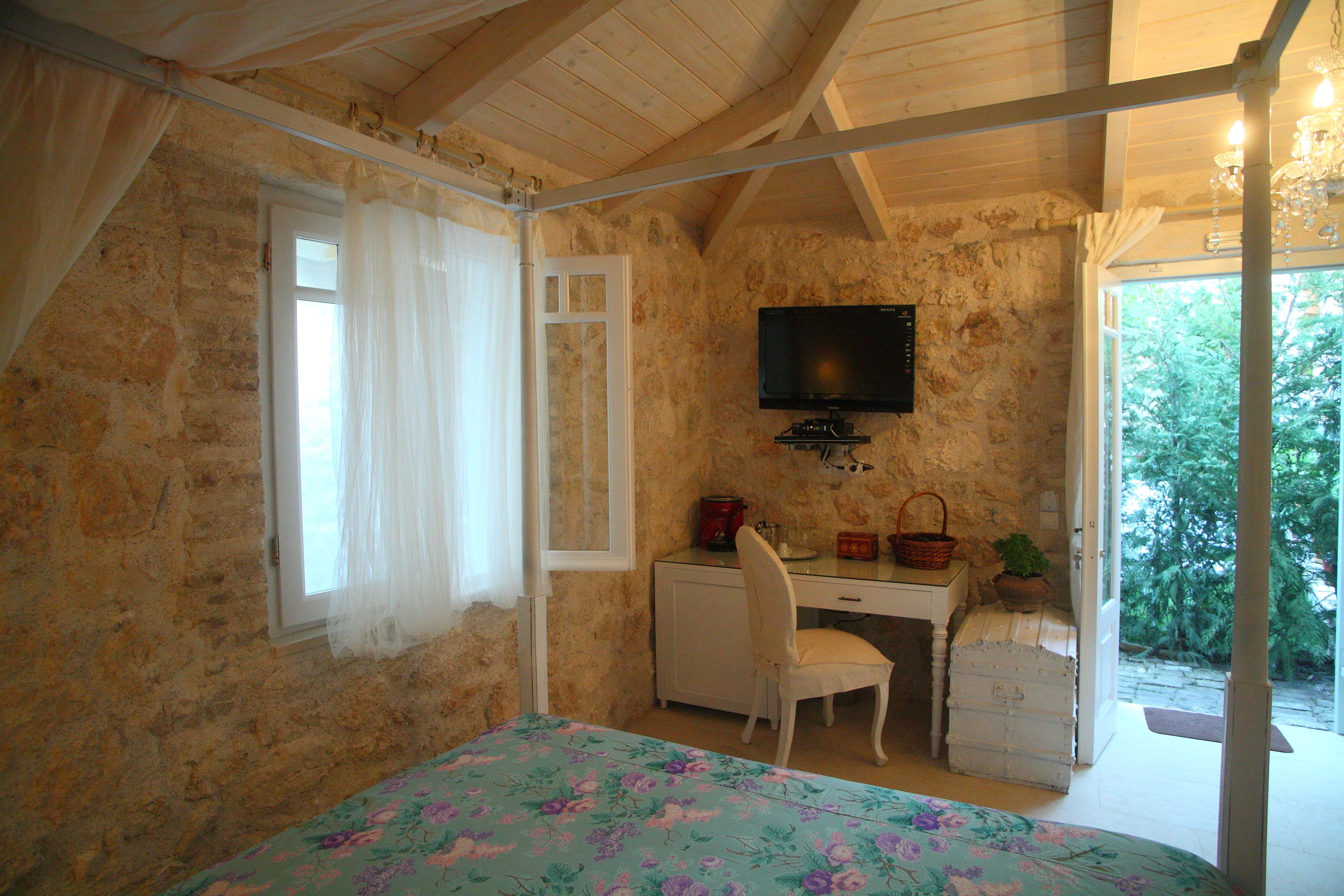 A bedroom with a bed, a desk, a chair, a television, and a window with curtains.