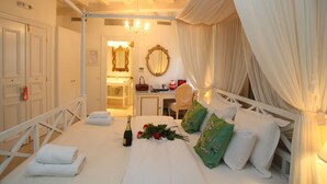Une chambre à coucher comprenant un lit, un bureau, une chaise, un miroir, et une salle de bain visible à travers une porte ouverte.