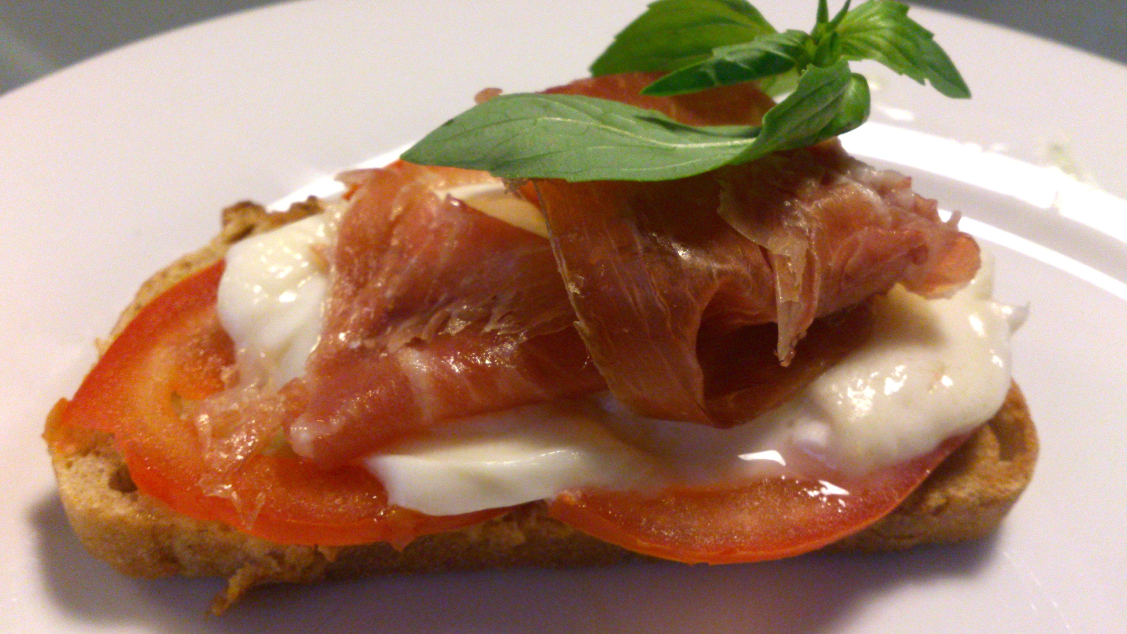 Sanduíche com tomate, queijo e presunto numa placa branca.