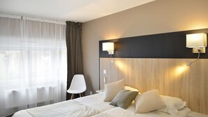 A hotel room with a large bed, two bedside tables, a chair, and a window with sheer curtains. - Au Site Normand (Clecy)