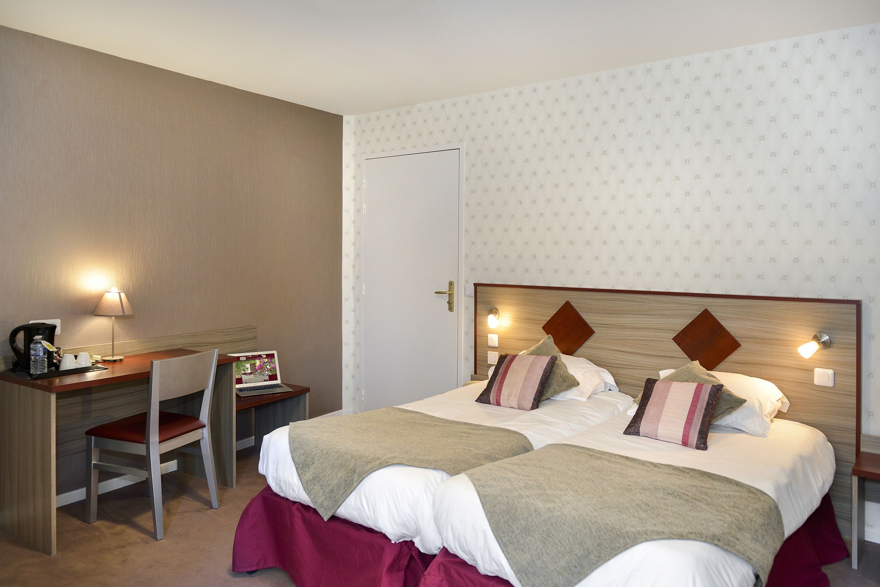 A hotel room with two beds, a desk with a chair, a laptop, and a coffee maker.