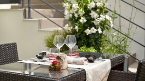 A dining table set with wine glasses, a candle, and a small bowl, surrounded by wicker chairs and a white tablecloth. - Au Site Normand (Clecy)