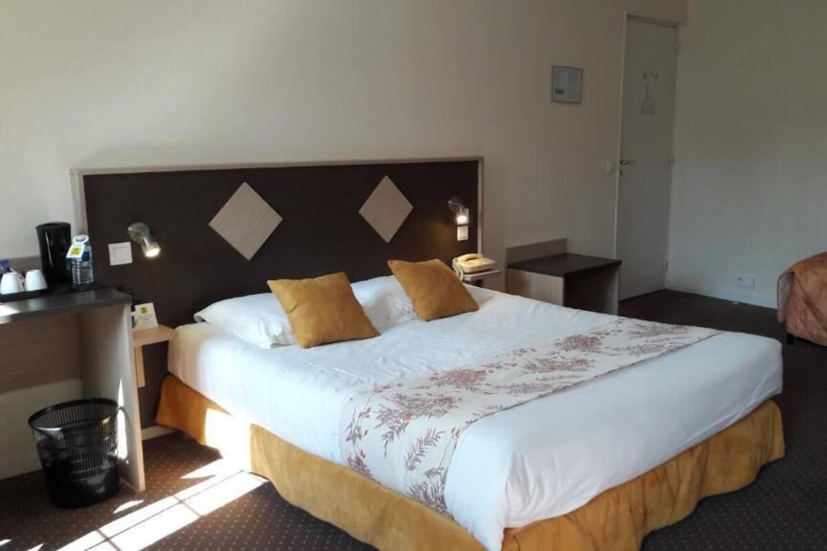 Una habitación de hotel con una cama grande, una mesita de noche con lámpara, un escritorio con silla y un cubo de basura.