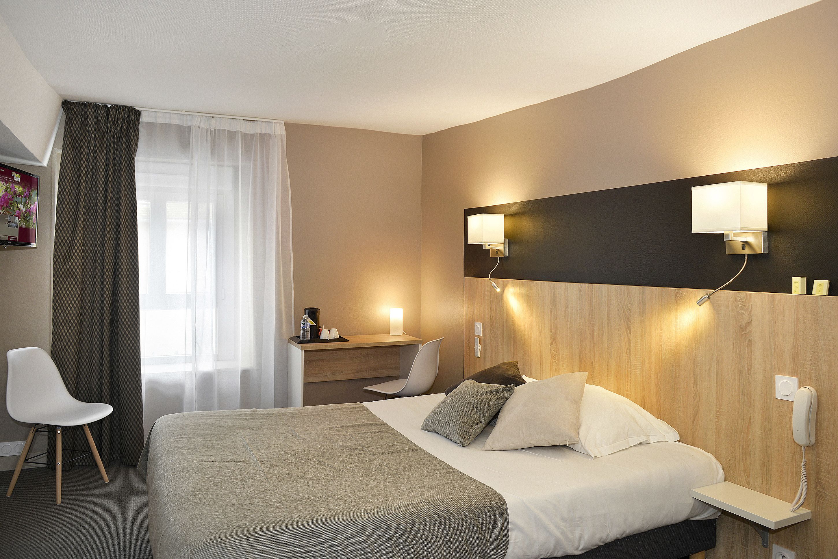 Et hotelværelse med seng, natbord, lampe, stol og et skrivebord med en computer.