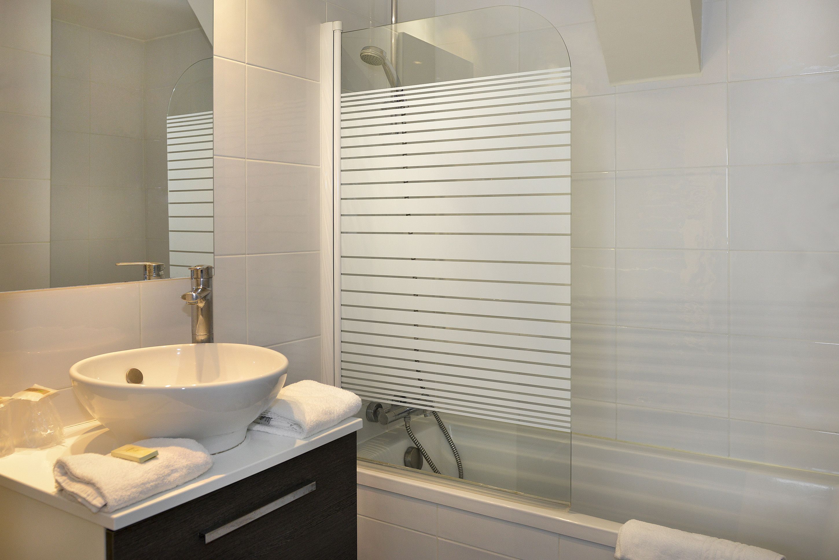 A modern bathroom with a large white sink, a glass shower enclosure, and a mirror above the sink.